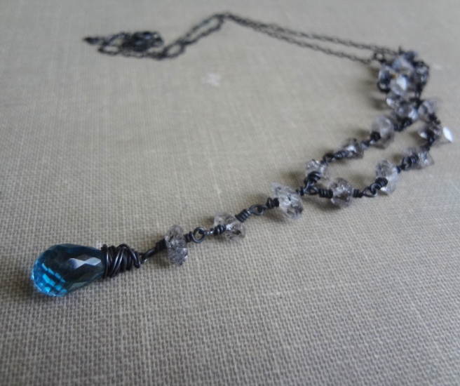 A blackened silver Y necklace with tiny Herkimer diamond crystals and a faceted London Blue topaz at the end wrapped with silver wire